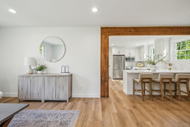 interior space with white cabinetry, kitchen peninsula, a breakfast bar, appliances with stainless steel finishes, and light wood-type flooring