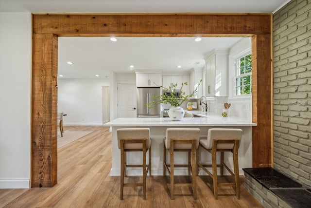 kitchen featuring high end refrigerator, kitchen peninsula, light hardwood / wood-style floors, white cabinetry, and brick wall