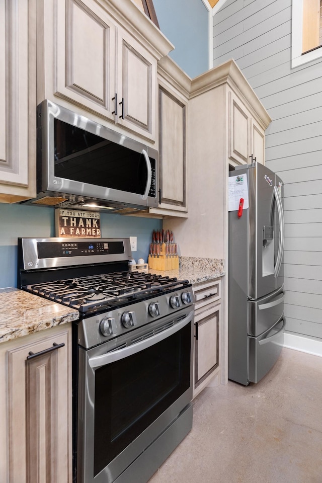 kitchen featuring cream cabinetry, light stone countertops, stainless steel appliances, and wooden walls