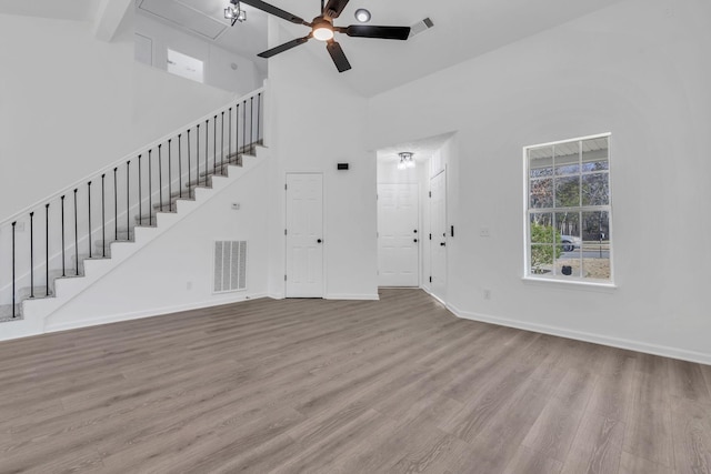 unfurnished living room featuring a towering ceiling, light hardwood / wood-style flooring, and ceiling fan