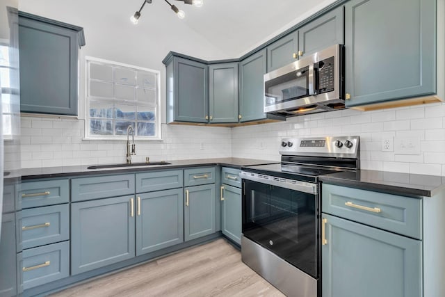 kitchen featuring sink, stainless steel appliances, light hardwood / wood-style flooring, backsplash, and lofted ceiling