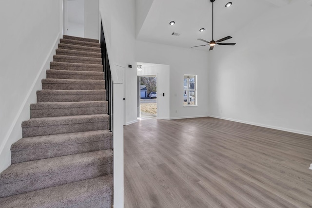 stairway with a high ceiling, hardwood / wood-style flooring, and ceiling fan