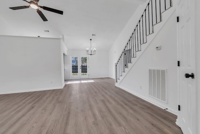 unfurnished living room featuring french doors, ceiling fan with notable chandelier, and light hardwood / wood-style flooring