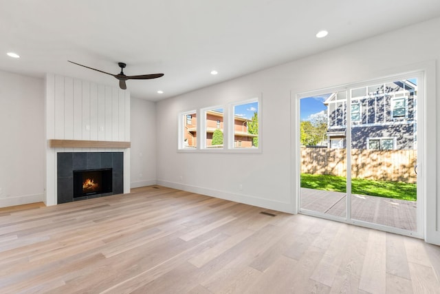 unfurnished living room featuring a tiled fireplace, ceiling fan, and light wood-type flooring