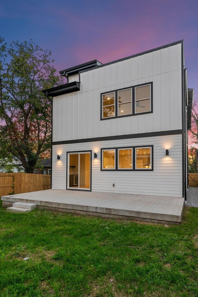 back house at dusk featuring a lawn and a patio area