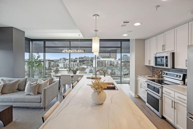 kitchen with sink, stainless steel appliances, a wall of windows, decorative light fixtures, and white cabinets