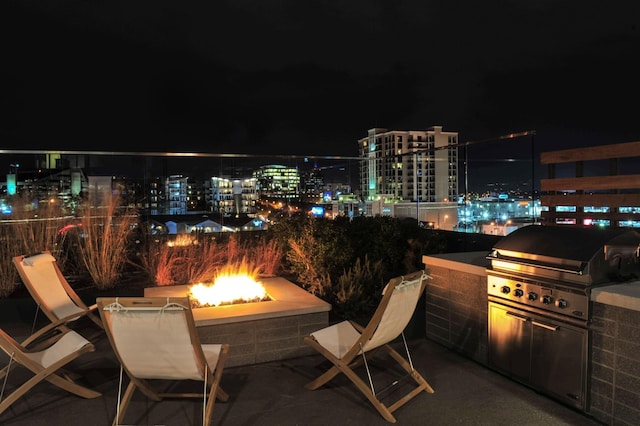 patio at night featuring grilling area, an outdoor fire pit, and exterior kitchen