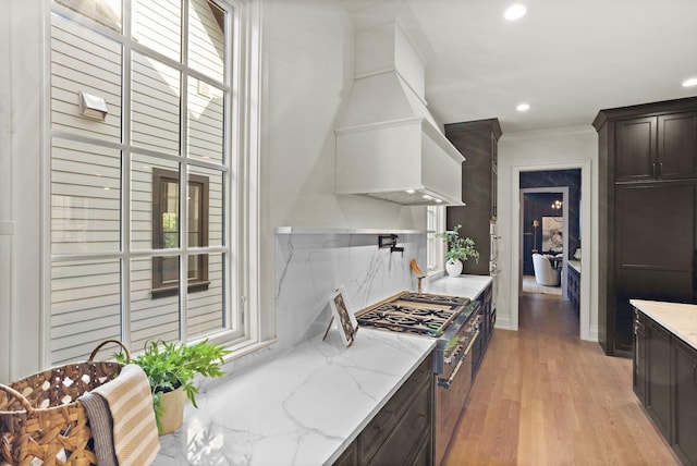 kitchen with backsplash, premium range hood, light stone countertops, high end stove, and ornamental molding