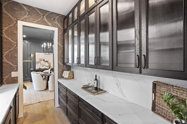 bar featuring a notable chandelier, dark brown cabinets, light wood-type flooring, and light stone countertops