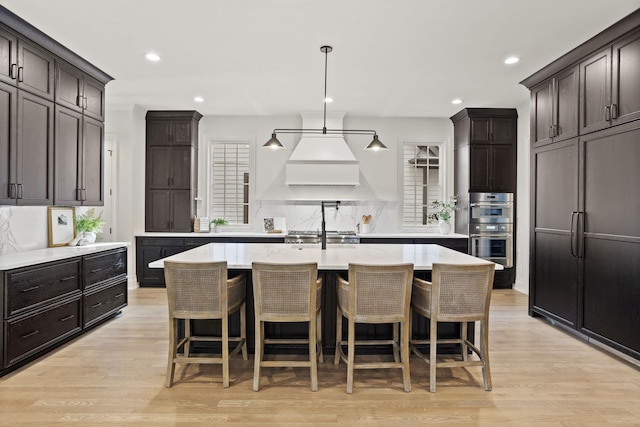 kitchen featuring hanging light fixtures, light wood-type flooring, double oven, and a kitchen island with sink