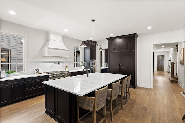 kitchen featuring premium range hood, a center island with sink, a kitchen breakfast bar, hanging light fixtures, and appliances with stainless steel finishes