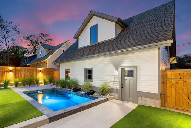 back house at dusk featuring a yard, pool water feature, and a fenced in pool