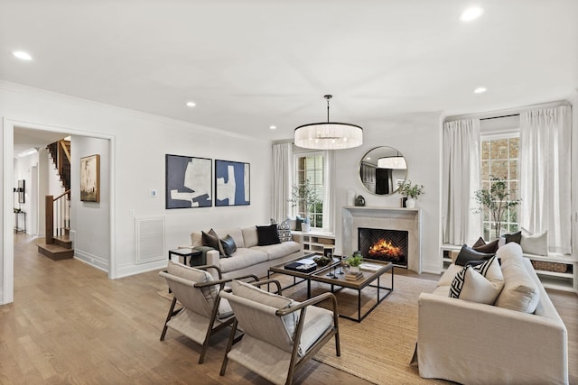 living room featuring a notable chandelier, a healthy amount of sunlight, ornamental molding, and light hardwood / wood-style flooring