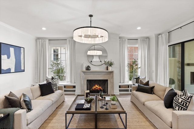 living room featuring a premium fireplace, ornamental molding, a chandelier, and light wood-type flooring