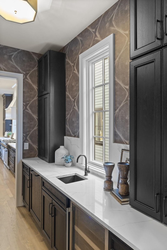 interior space with light stone countertops, light hardwood / wood-style floors, wine cooler, and sink