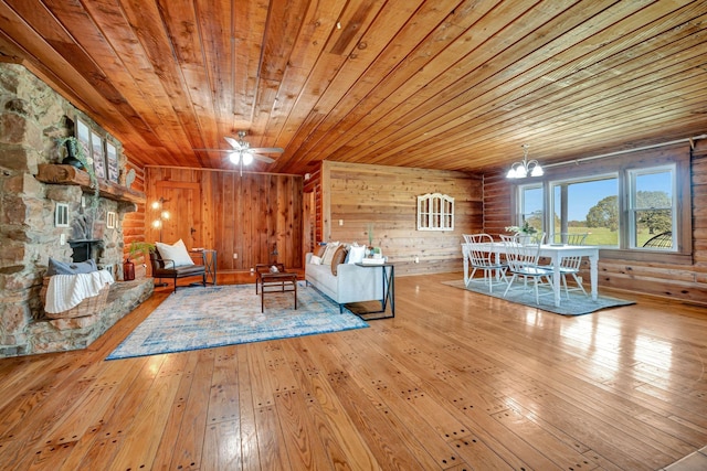 unfurnished living room featuring wooden ceiling, ceiling fan with notable chandelier, a stone fireplace, wooden walls, and light hardwood / wood-style floors