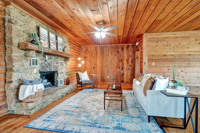 living room featuring rustic walls, wood ceiling, ceiling fan, hardwood / wood-style floors, and a stone fireplace