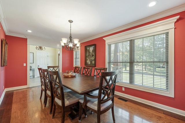 dining space featuring wood-type flooring, ornamental molding, and an inviting chandelier