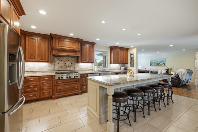 kitchen with a center island, light stone countertops, appliances with stainless steel finishes, tasteful backsplash, and a kitchen bar