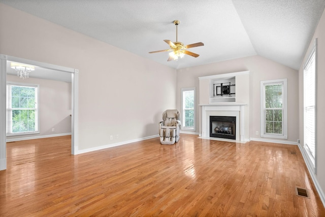 unfurnished living room featuring ceiling fan with notable chandelier, light hardwood / wood-style floors, a textured ceiling, and vaulted ceiling