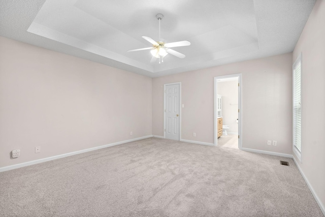 empty room featuring a tray ceiling, ceiling fan, and light colored carpet