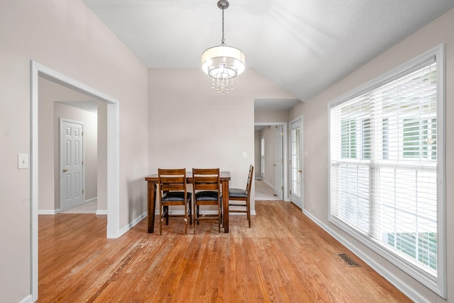 dining space with light hardwood / wood-style floors, vaulted ceiling, and a notable chandelier