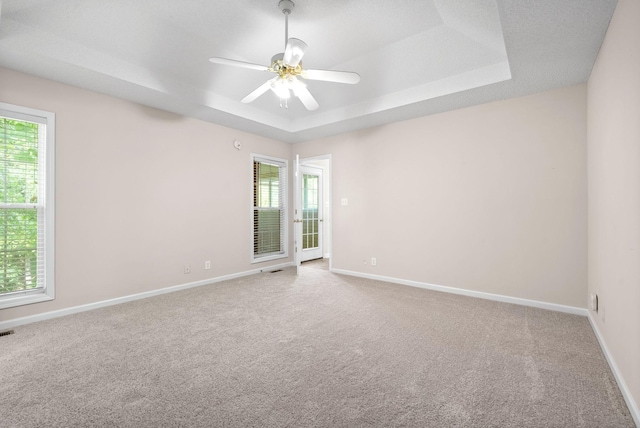 carpeted spare room with ceiling fan, a wealth of natural light, and a tray ceiling