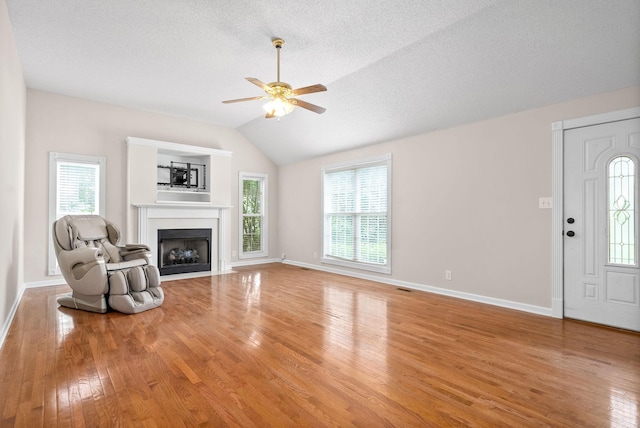 unfurnished living room with ceiling fan, light hardwood / wood-style floors, a wealth of natural light, and vaulted ceiling