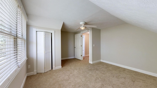 unfurnished bedroom featuring a textured ceiling, lofted ceiling, light carpet, ceiling fan, and a closet