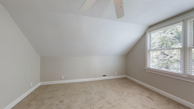 additional living space featuring a textured ceiling, ceiling fan, vaulted ceiling, and light colored carpet