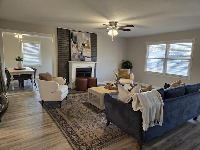 living room featuring a large fireplace, hardwood / wood-style flooring, ceiling fan, and plenty of natural light