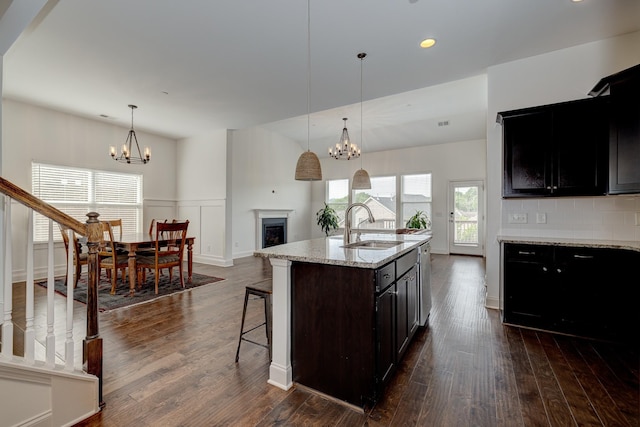 kitchen featuring pendant lighting, a kitchen island with sink, sink, a notable chandelier, and light stone counters