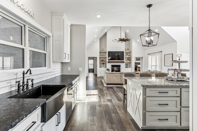 kitchen featuring sink, dark stone countertops, decorative light fixtures, lofted ceiling, and white cabinets