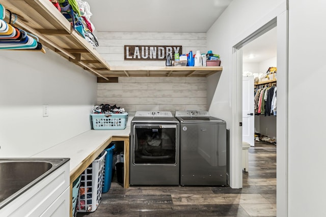 clothes washing area with washer and dryer, dark hardwood / wood-style flooring, sink, and wood walls