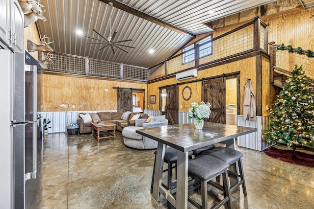 dining room with wood walls, high vaulted ceiling, ceiling fan, a barn door, and a wall mounted AC