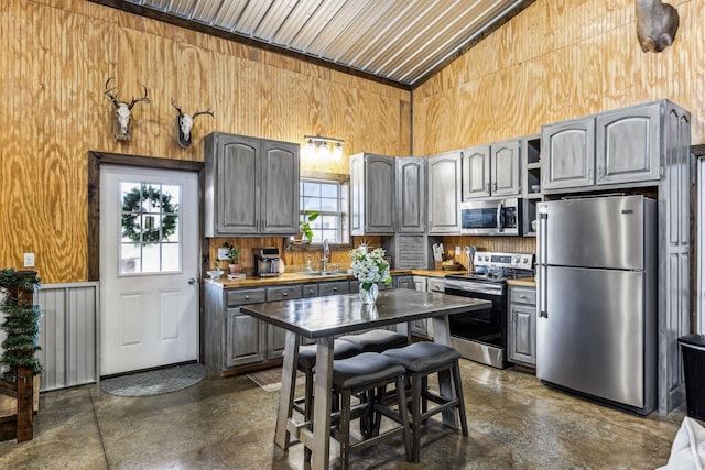 kitchen featuring gray cabinetry, wooden walls, sink, and appliances with stainless steel finishes