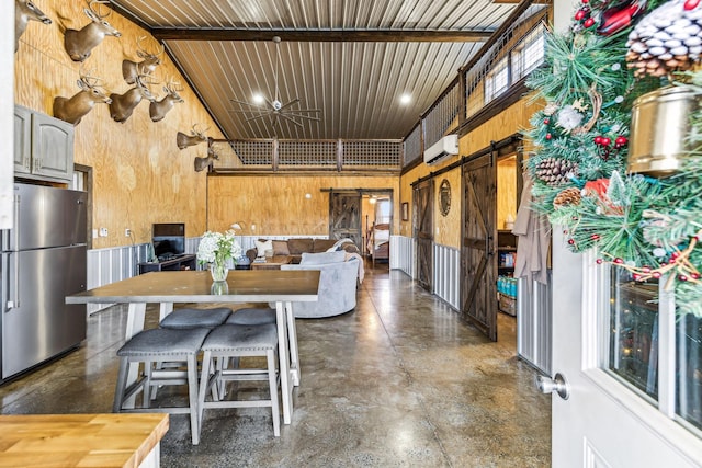 kitchen with stainless steel fridge, beam ceiling, a barn door, high vaulted ceiling, and wood walls