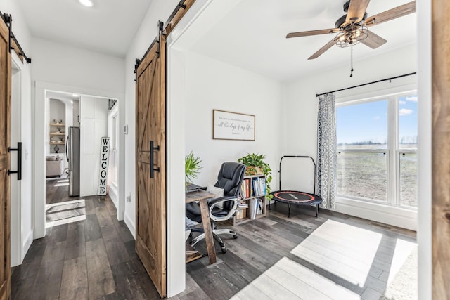 home office featuring ceiling fan, a barn door, and dark wood-type flooring