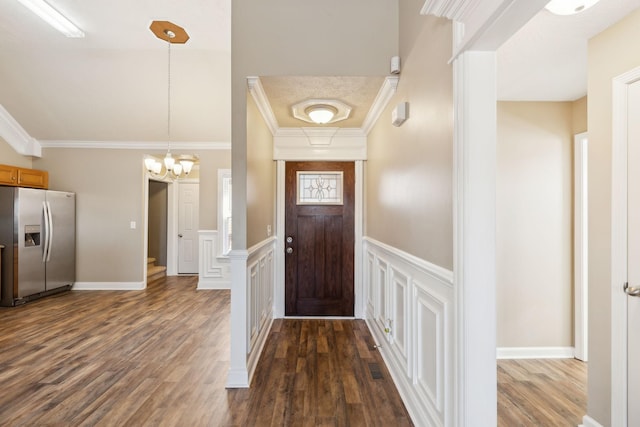 entryway with an inviting chandelier, dark wood-type flooring, and ornamental molding