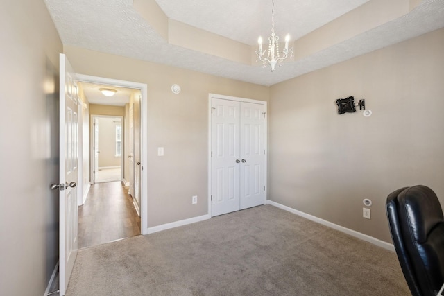 unfurnished office featuring a raised ceiling, light colored carpet, a textured ceiling, and a notable chandelier