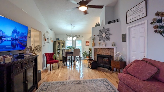 living room featuring a fireplace, light hardwood / wood-style flooring, ceiling fan with notable chandelier, and vaulted ceiling