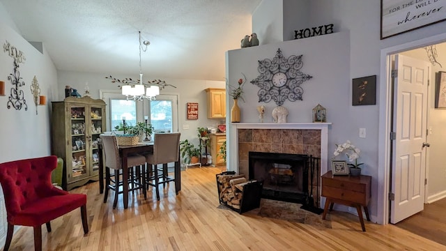 dining area with a fireplace, a textured ceiling, light hardwood / wood-style floors, and a notable chandelier