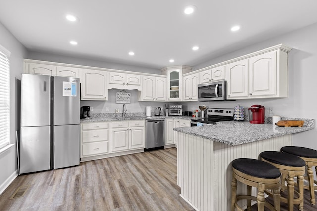 kitchen featuring light wood-type flooring, appliances with stainless steel finishes, kitchen peninsula, light stone countertops, and white cabinets