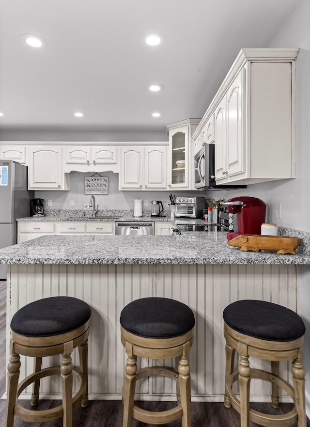 kitchen with white cabinetry, sink, kitchen peninsula, stainless steel appliances, and light stone countertops