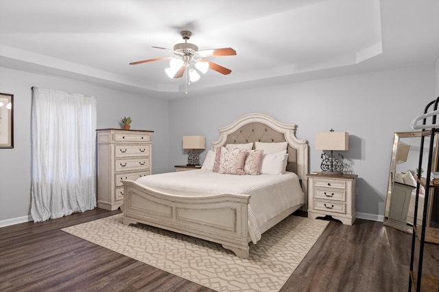 bedroom featuring a raised ceiling, dark wood-type flooring, and ceiling fan