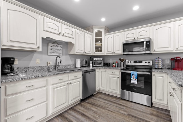 kitchen featuring sink, white cabinets, stainless steel appliances, light stone countertops, and dark wood-type flooring