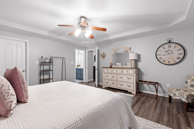 bedroom with ensuite bath, dark wood-type flooring, a raised ceiling, and ceiling fan