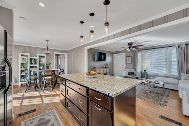 kitchen with open floor plan, dark brown cabinets, a center island, stainless steel fridge, and decorative light fixtures