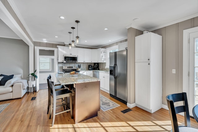 kitchen featuring decorative light fixtures, crown molding, appliances with stainless steel finishes, white cabinets, and light stone countertops