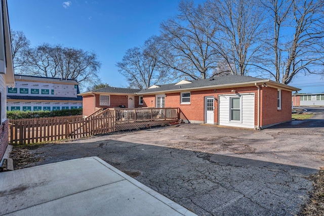 back of house featuring a patio, aphalt driveway, brick siding, fence, and a wooden deck